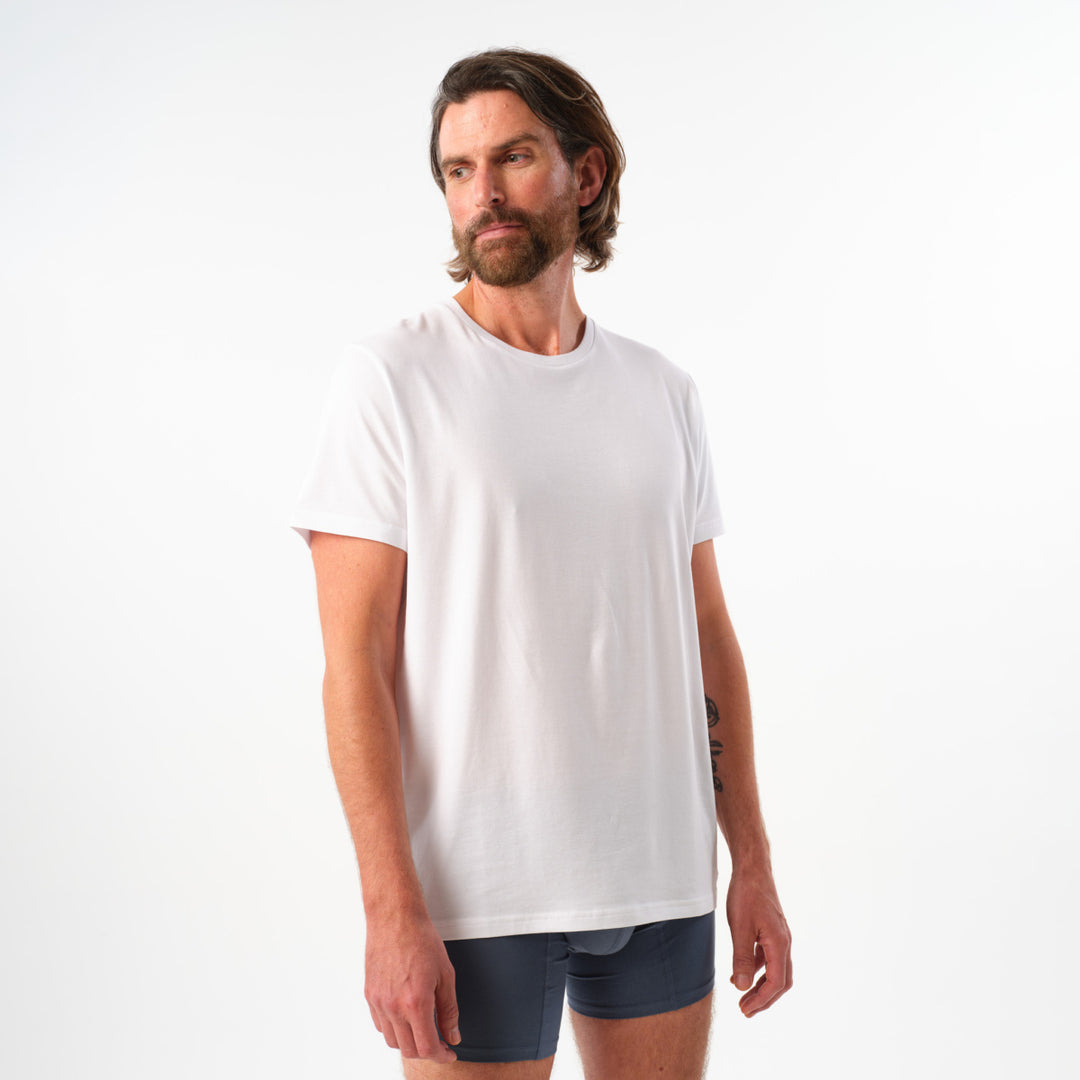 Man wearing a plain white t-shirt and dark shorts on a light gray background